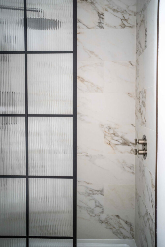 Marble tiled shower with black edged shower screen at The Priory in Tetbury, Cotswolds